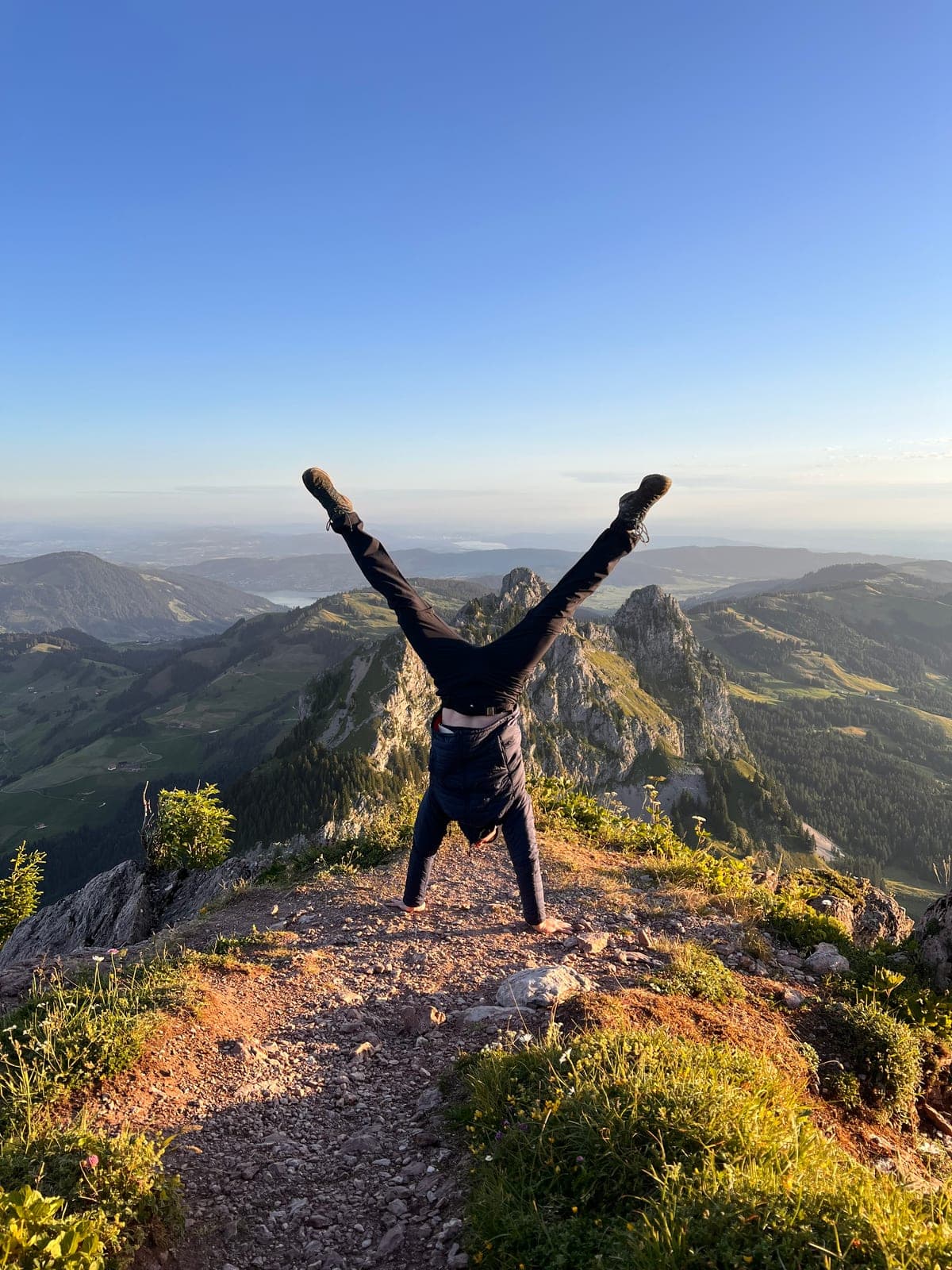 Jannis macht einen Handstand auf einem Berggipfel, im Hintergrund das Tal.